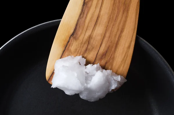 Кокосовое масло на деревянной лопаточкой над тефлоновой сковороде — стоковое фото