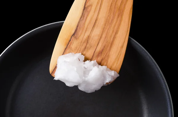 Coconut oil on wooden spatula over coated pan — стоковое фото