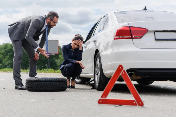 Businessman Gesturing Sad Businesswoman Squatting Broken Car Road — стоковое фото